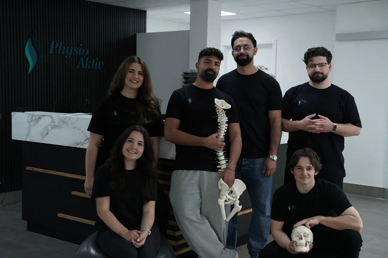 Das Team von PhysioAktiv am Empfangstresen, mit einem Wirbelsäulen- und einem Schädelmodell